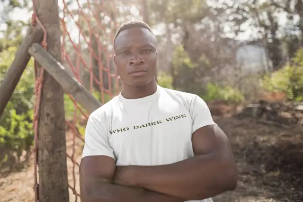 Model wearing a white triblend t-shirt with the bold Who Dares Win; design, styled casually to highlight its luxurious look and comfortable fit, available in sizes S-3XL